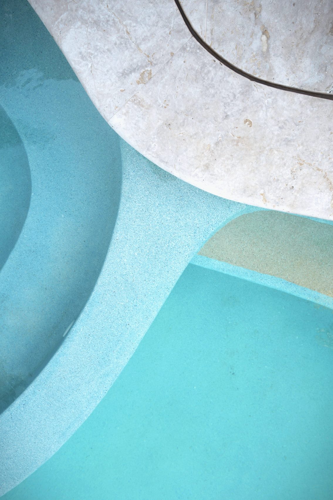 Curved turquoise pool meeting pale travertine stone
